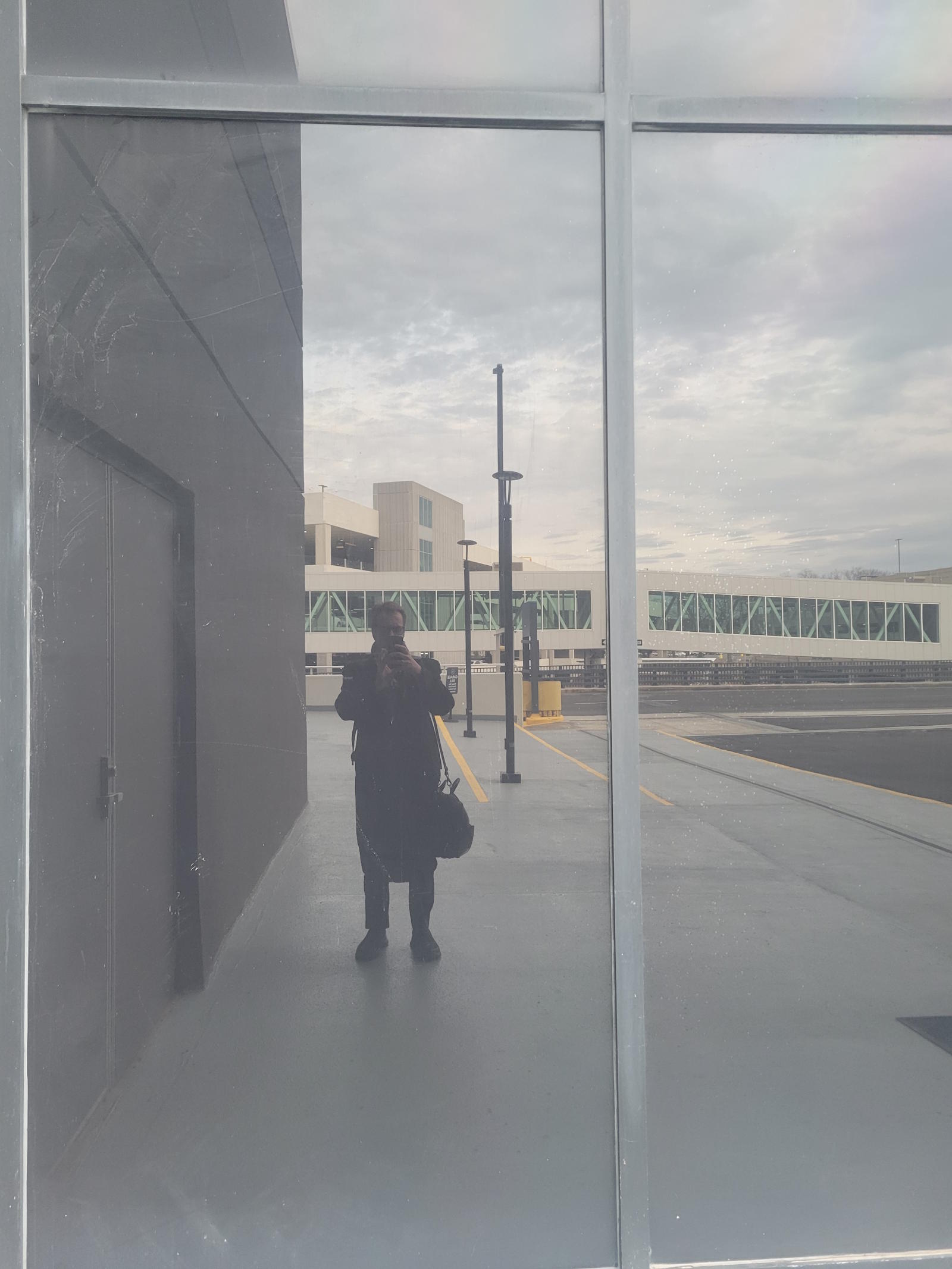 Artist's reflection in airport terminal glass at Bradley International Airport, March 30 2026 - the closing image of What Water Remembers