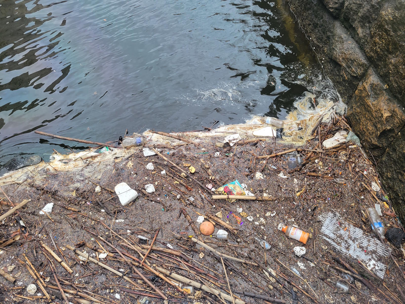 Debris and waste accumulated at the Providence River's edge against rocks, March 27 2026
